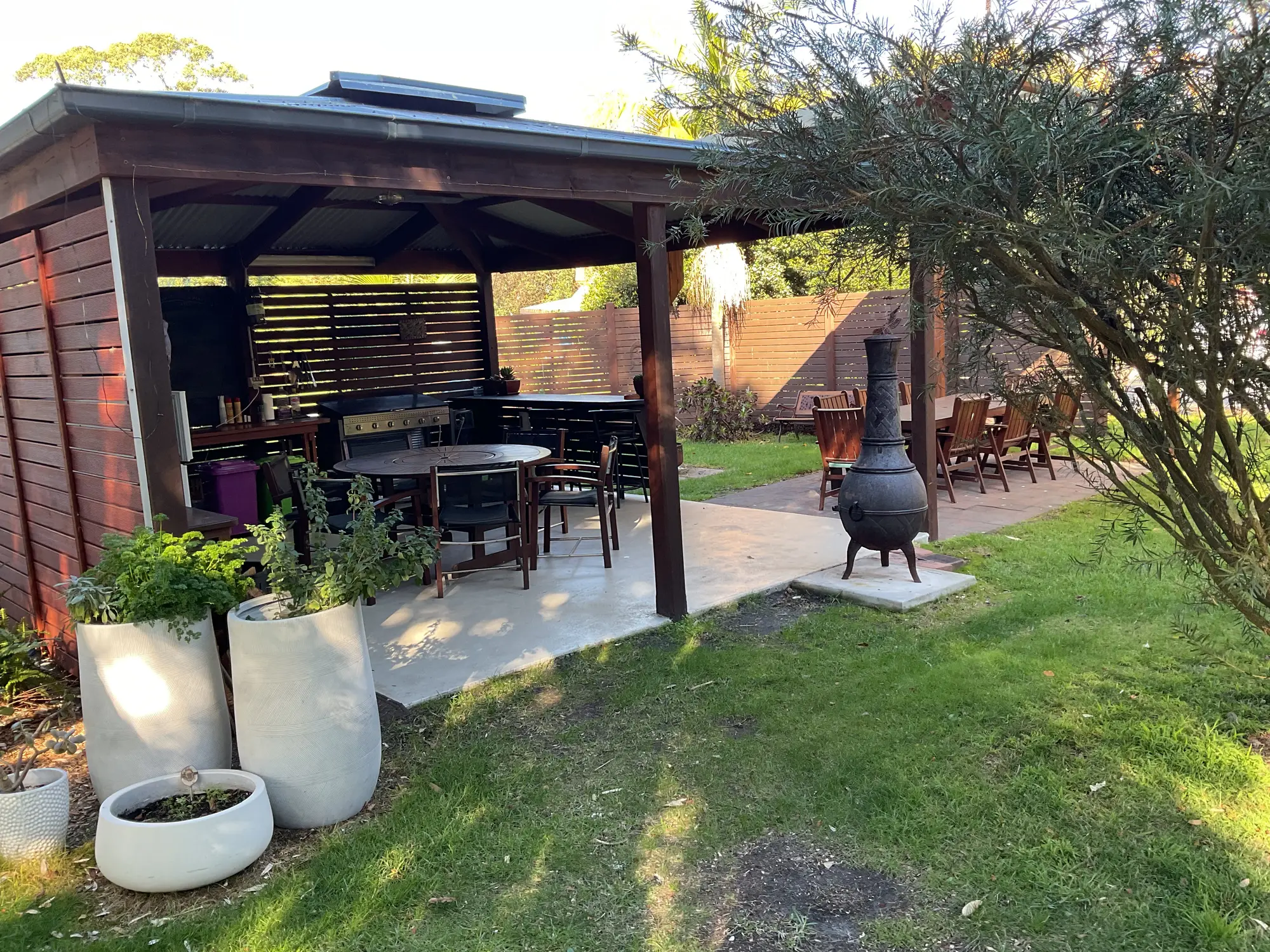 Covered BBQ pavilion with outdoor dining, herb pots and a chiminea